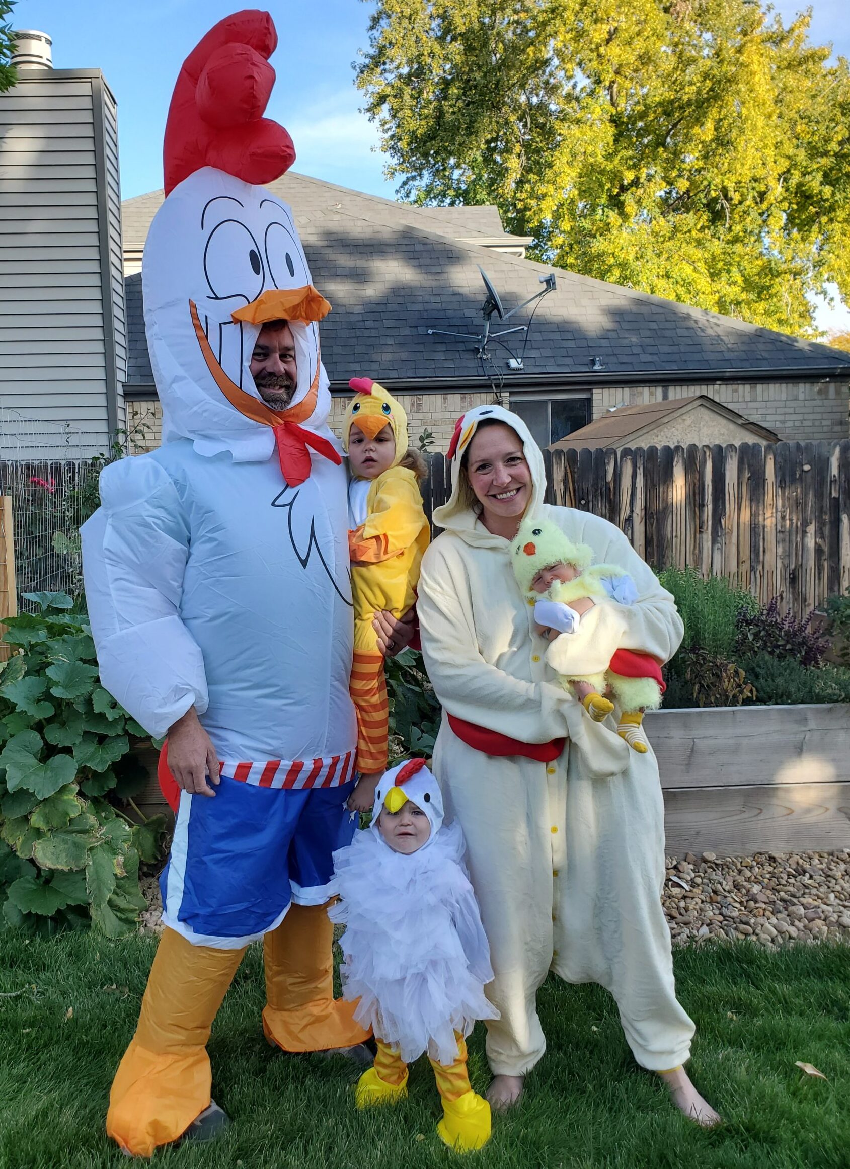 Two adults and three children. One adult and one child are in a white body outfit, red feathers on head and yellow beak and feet. The other adult and two of the children are all wearing yellow onesies, with red feathers on head and orange beak.