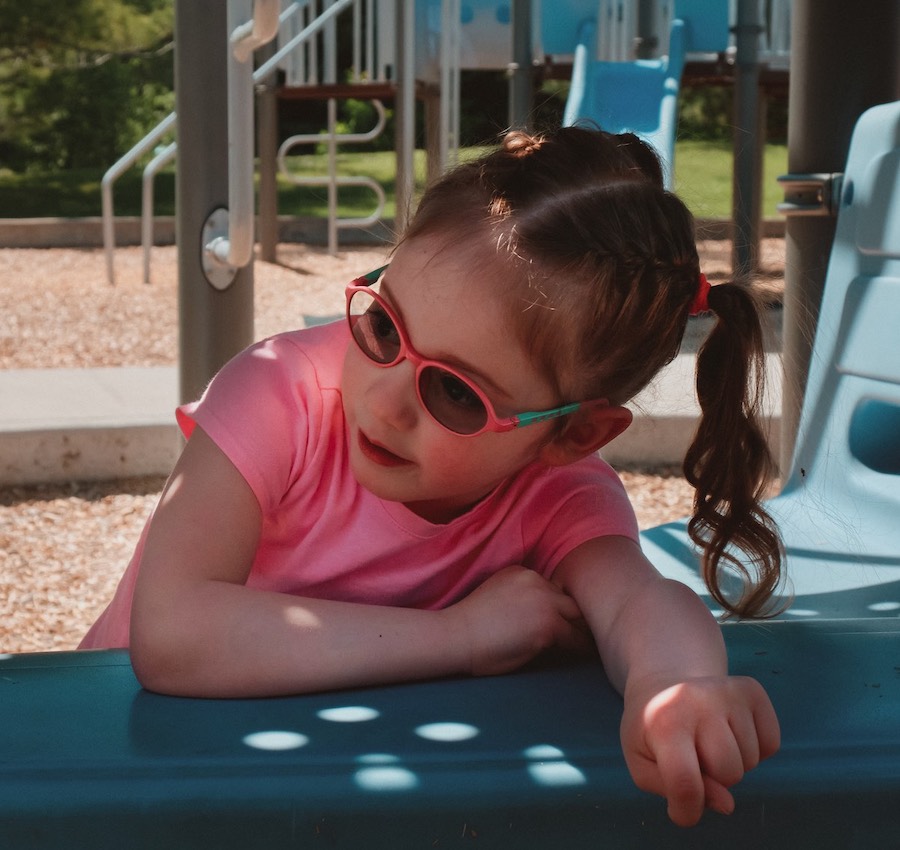 A young girl in glasses playing on a playground, looking at someone off camera.