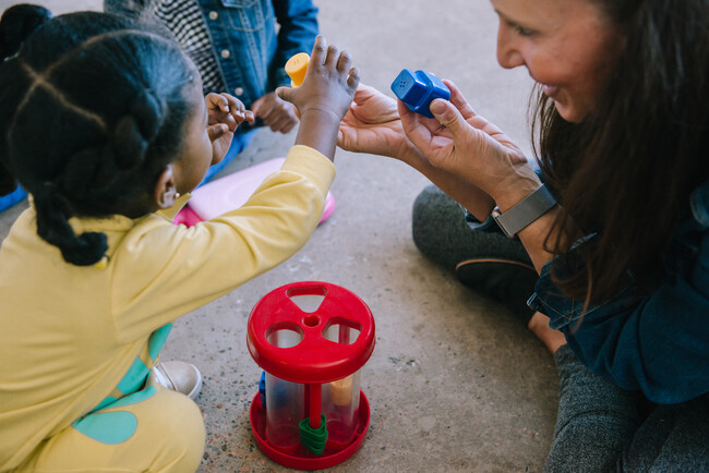 Caregiver smiling playing with a toy with a young black girl