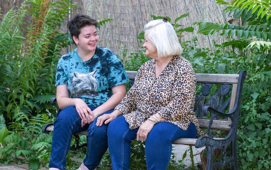 Mom and adult daughter sitting on a park bench looking at each other smiling