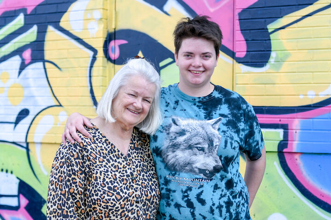 Adult daughter in a tie die shirt with arm around her mom smiling