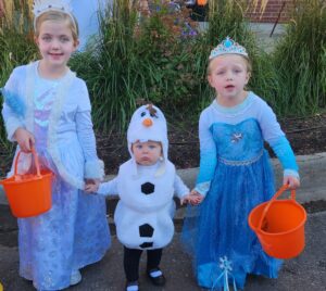 Three children dressed from the movie Frozen in blue and white dresses. The child in the middle is dressed as Olaf the snowman.