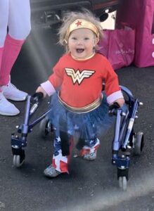Child dressed as superwoman with a gold headband and red star, a red top, and blue tutu.