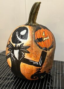 Pumpkin painted with a black Jack Skellington holding an orange pumpkin.
