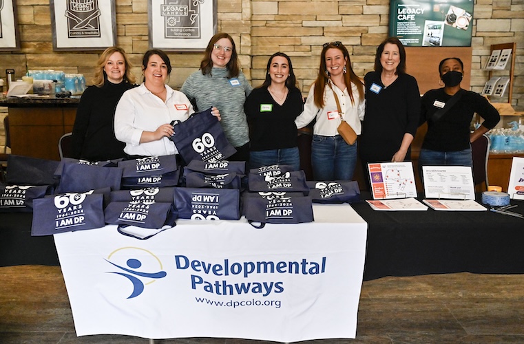 7 woman smiling standing behind a table with DP bags displayed
