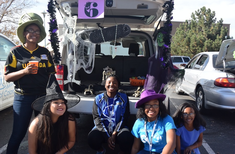 Kids and teens in halloween hats smiling sitting behind a car
