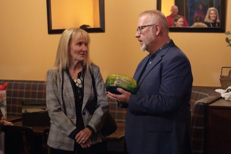 Woman in blond hair accepting a thank you gift from a man in a suit