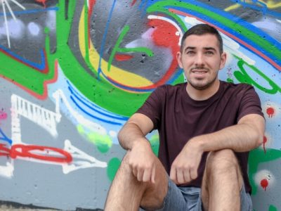 Man smiling leaning against a graffiti wall